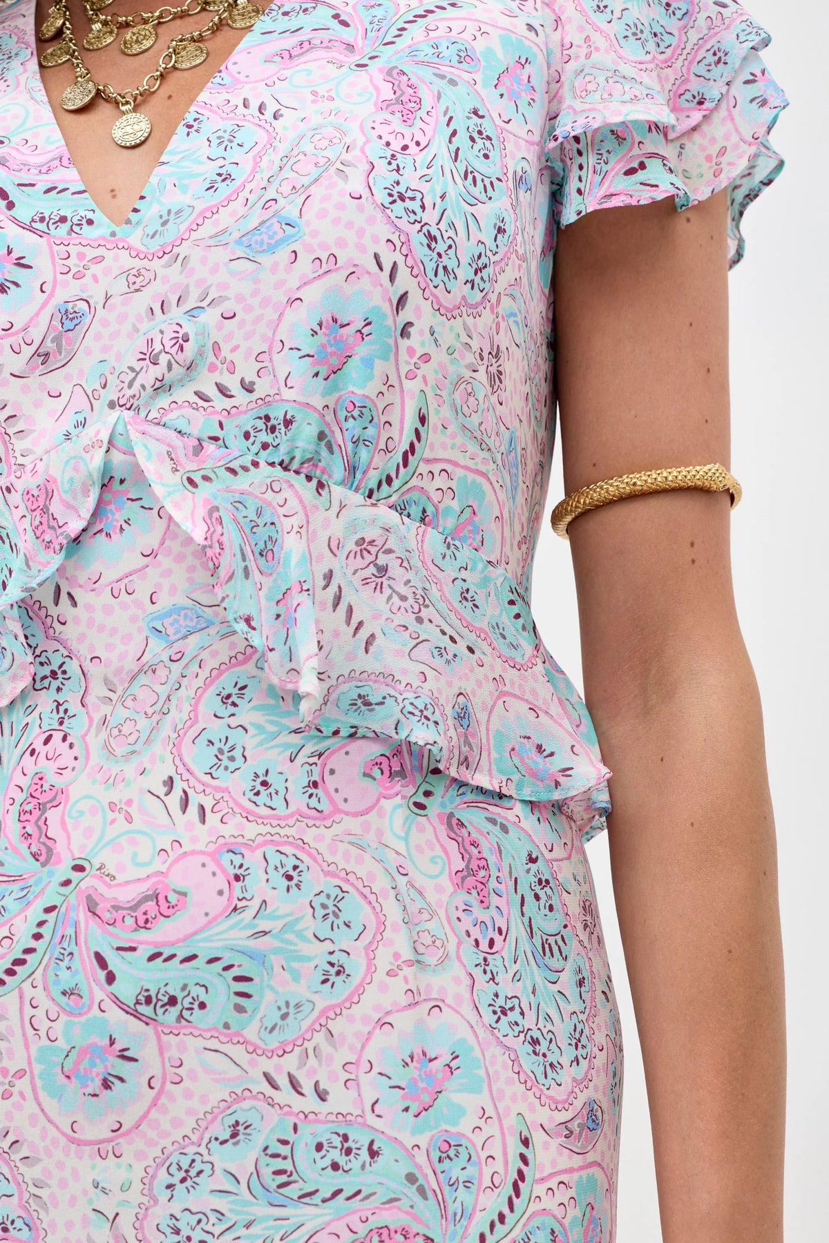 A person wearing the Thanvi - Butterfly Paisley Cream summer dress with ruffled details, layered gold necklace, and gold arm cuff. Only the upper torso and part of the right arm are visible.