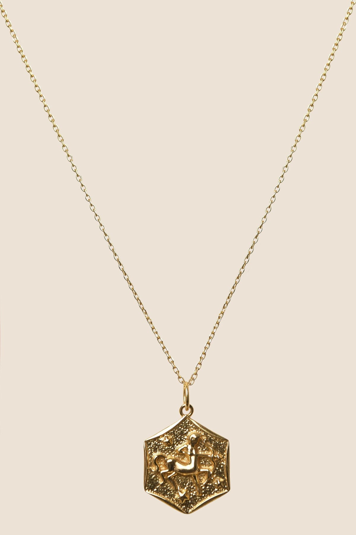 A gold vermeil necklace with a delicate chain and a hexagonal pendant featuring intricate patterns and Arabic script, displayed on a beige background—Zodiac - Sagittarius, a unique addition to any collection of Zodiac necklaces.