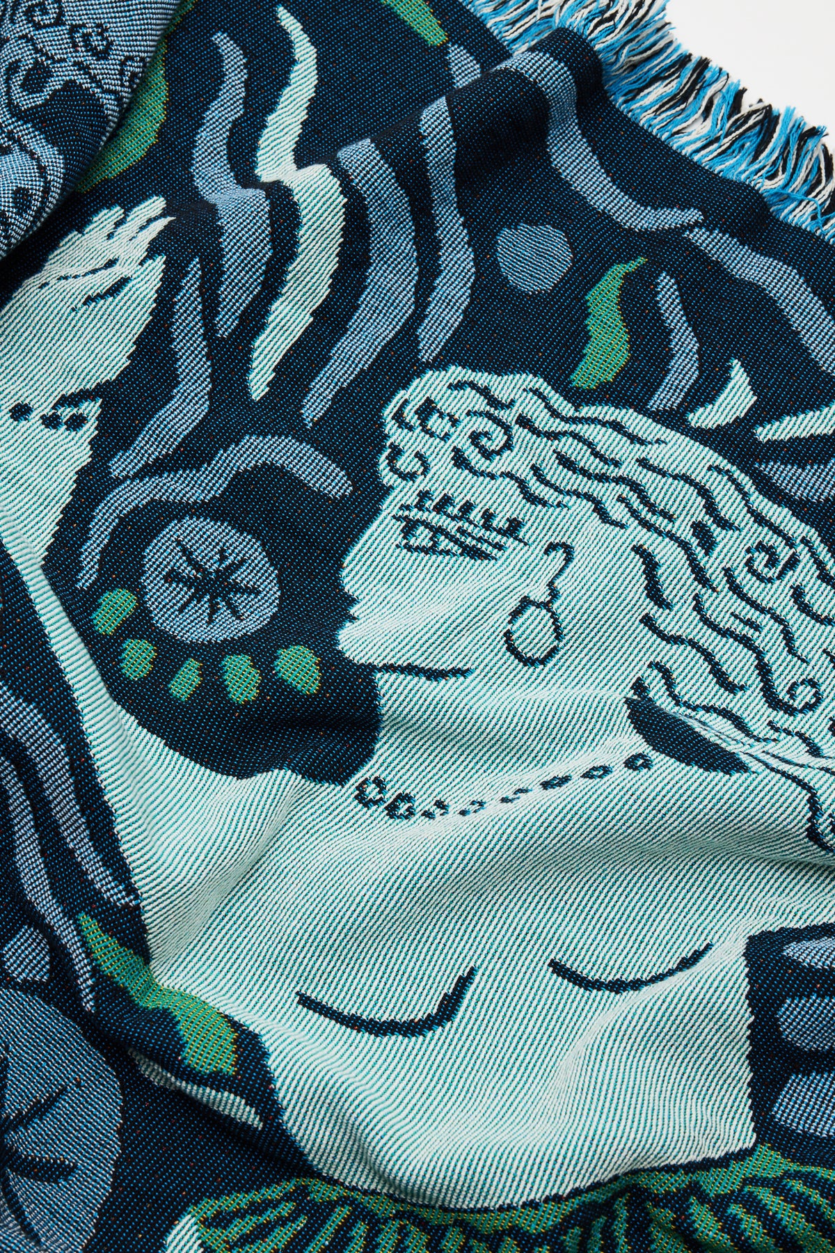 The Mythos Throw - Navy from the Mythos Collection features an abstract design depicting a person with flowing hair, an earring, and a raised arm, set amidst wavy lines and leaf motifs in blue, green, and white tones. Inspired by Greek mythology, this distinctive woven textile seamlessly blends traditional elements with contemporary flair—making it an ideal choice for those who appreciate artistic woven throws.