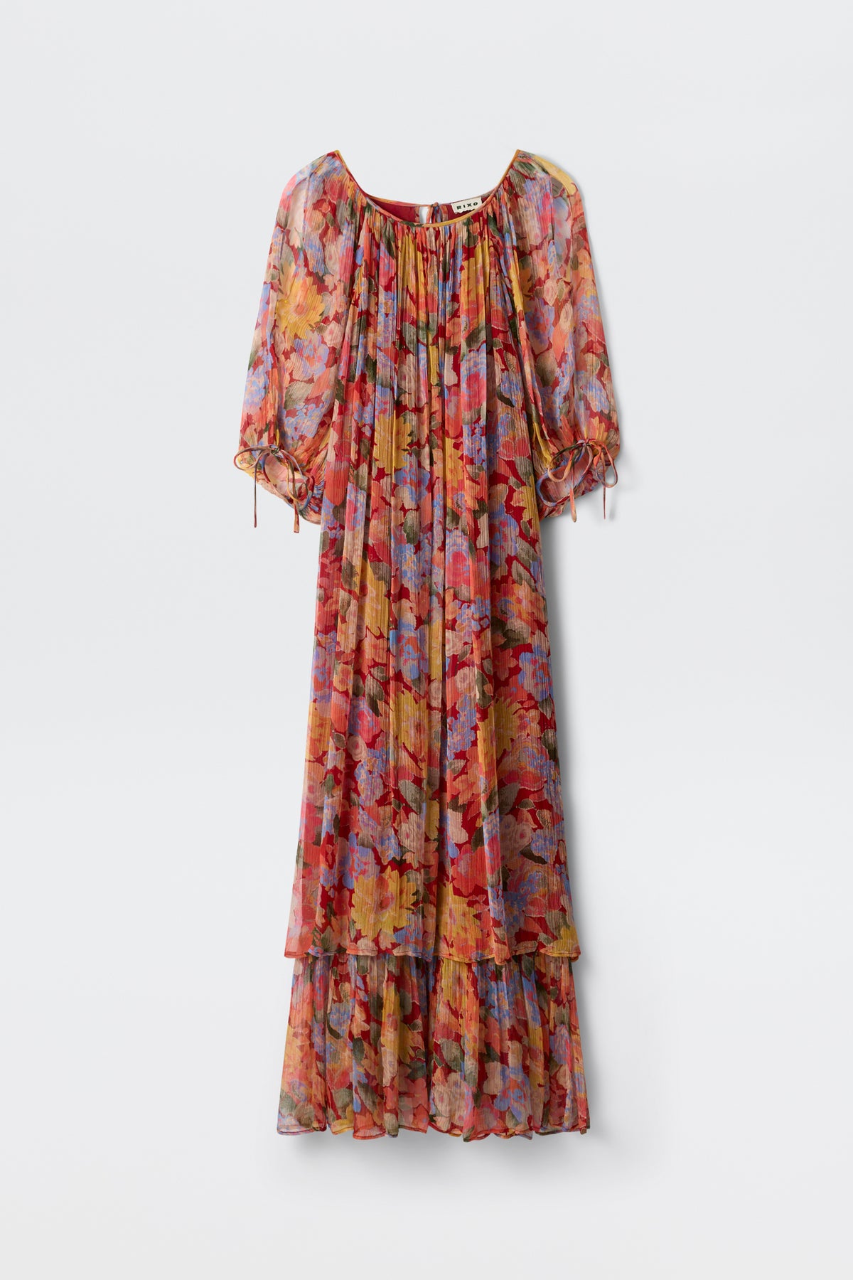 The Hayden - Chelsea Floral Red is a long, flowy dress adorned with a vibrant floral pattern in shades of red, orange, blue, and purple. It features puffed half sleeves and a ruffled hem and is displayed against a plain white background.