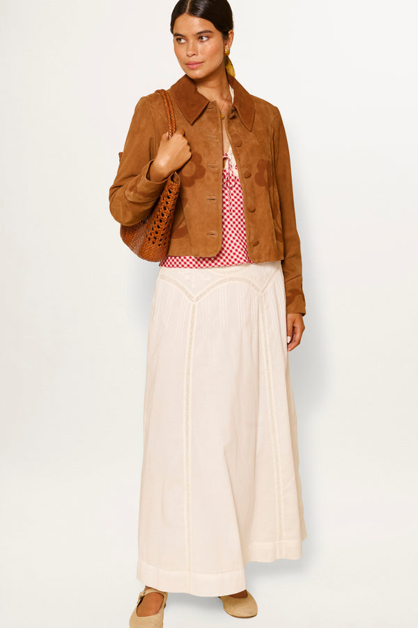Woman wearing the Vienne - Pansy Embroidery Ivory vintage-inspired white skirt with a brown suede jacket, red and white patterned top, beige shoes, and holding a brown woven bag against a plain white background.