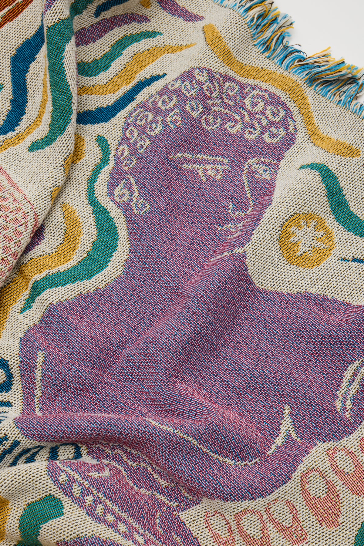 The Athena Throw - Ivory from the Mythos Collection features a stylized purple profile inspired by Greek mythology, set among abstract yellow, teal, and pink patterns, with visible fringe along the edges.