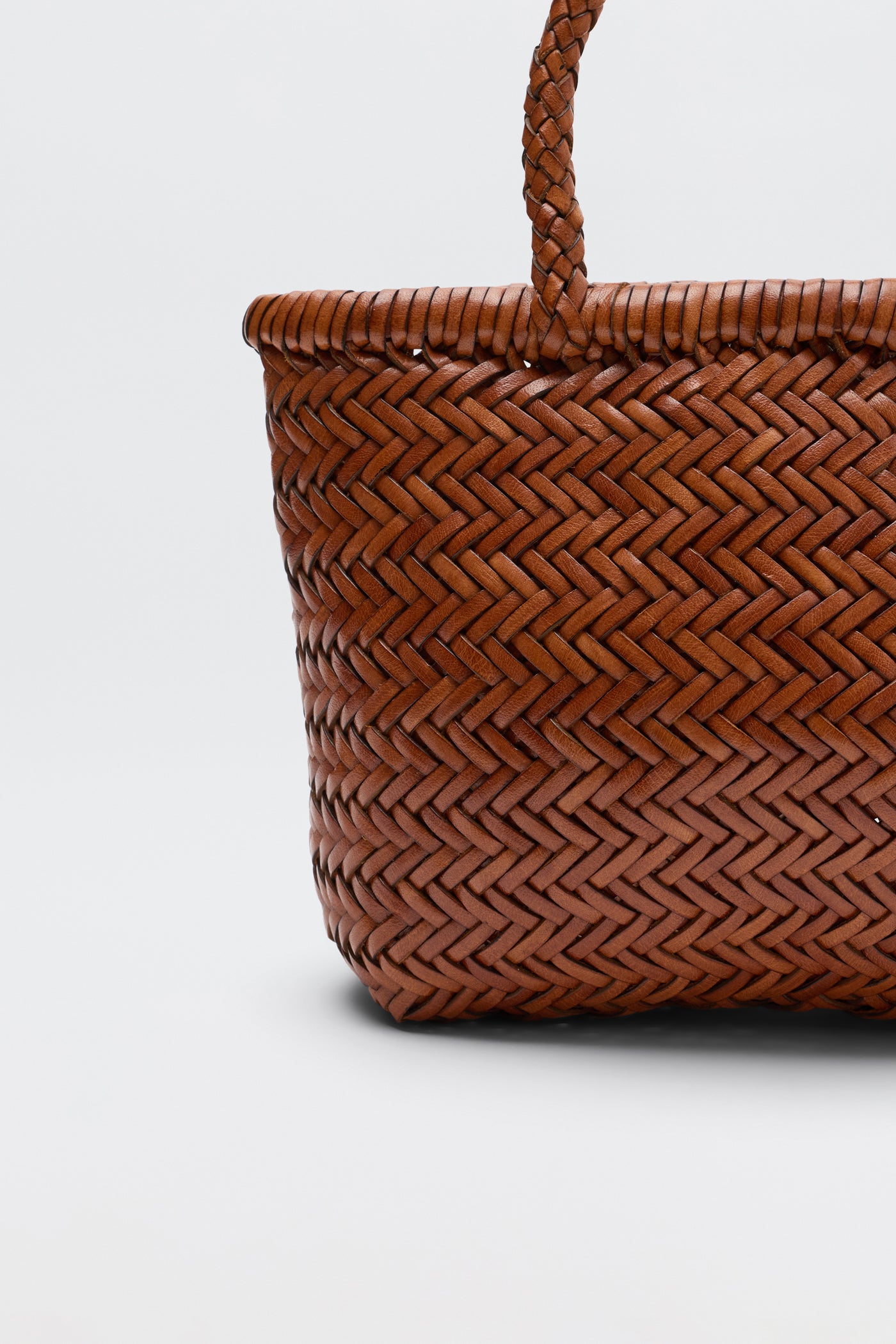 Close-up of the Lysia - Tan basket with a braided handle, showcasing its detailed herringbone pattern in a warm brown hue against a plain white background. Reminiscent of vintage woven bags, this piece combines timeless style with modern craftsmanship.